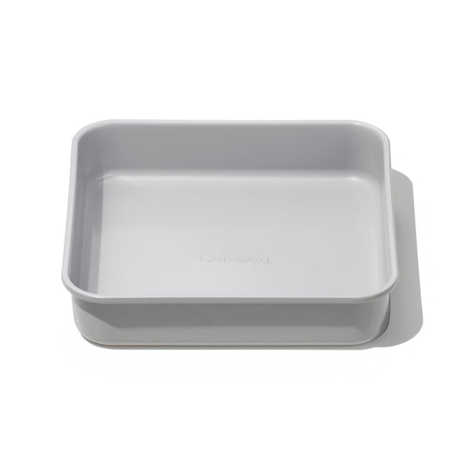 The Caraway Square Cake Pan, 9 in light gray boasts a non-toxic ceramic coating and smooth edges. Its simple design and non-stick feature make it oven safe and ideal for baking, beautifully displayed against a crisp white background.