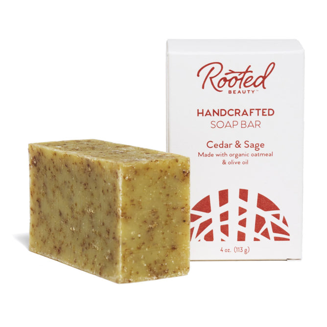 The 4 oz (113 g) bar of Cedar & Sage soap, crafted from organic oatmeal and olive oil, features a speckled design and sits beside a white box branded with Rooted Beauty. This moisturizing soap is also cruelty-free.