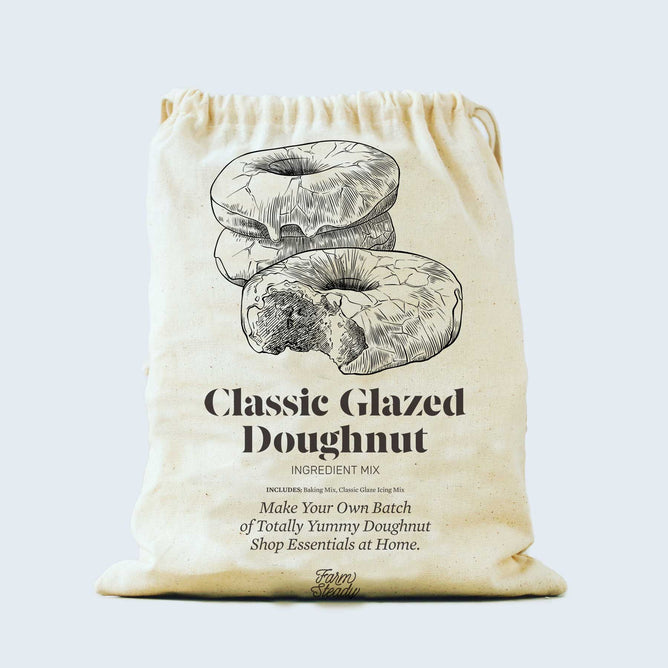 A beige drawstring bag displays a sketch of two glazed doughnuts, one bitten, with text: Classic Glazed Doughnut Baking Mix by FarmSteady, inviting easy homemade doughnut creation.