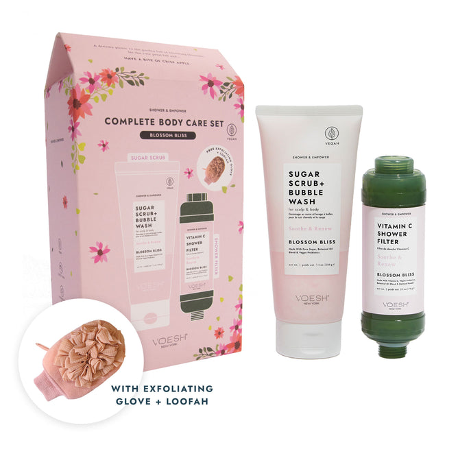 The image displays a VOESH New York Complete Body Care Set in Blossom Bliss scent, including a sugar scrub + bubble wash, a vitamin C shower filter, and an exfoliating glove. The packaging features pink floral designs, highlighting its blend of beauty and care.