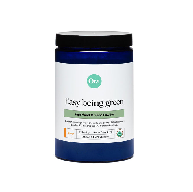 A blue container labeled Easy Being Green: Daily Active Superfood Greens by Ora Organic holds a digestion-support superfood greens powder. The white label with green accents indicates 30 servings, a net weight of 8.5 oz (240g), and an orange flavor, marked as a dietary supplement.