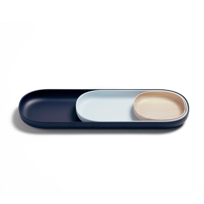 The Open Spaces Nesting Tray Set features three trays: the largest is dark blue, the middle is light blue, and the smallest is wooden, arranged on a white surface for an organized, minimalist display.