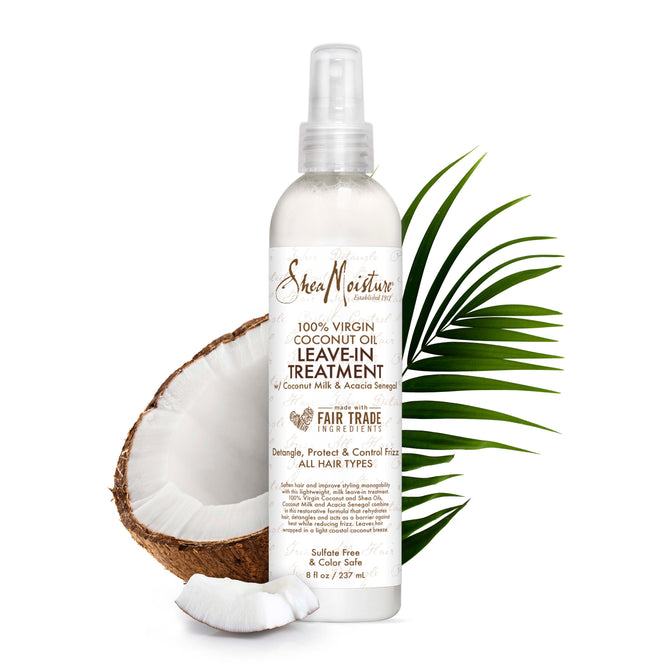 Displayed with a halved coconut and lush palm leaves, the SheaMoisture 100% Virgin Coconut Oil Daily Hydration Leave-In Treatment features a sleek white bottle with brown text and a spray nozzle, designed to detangle, protect, and control frizz for all hair types.