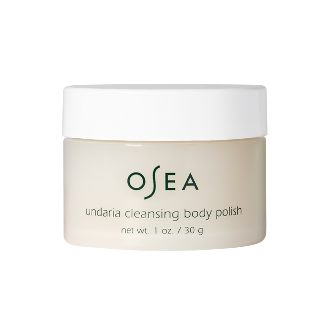 A sleek white jar of OSEAs Undaria Cleansing Body Polish - Travel Size displays its name and 1 oz (30 g) net weight on a simple label. Enriched with Undaria seaweed, this AHA exfoliation product highlights its transformative gel-to-milk formula against a plain white background.
