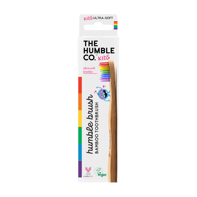 The image displays The Humble Co. Kids Bamboo Toothbrush, which is dentist-approved with ultra-soft nylon bristles. The packaging is white with rainbow accents and cartoon fish graphics, featuring cruelty-free and vegan logos.