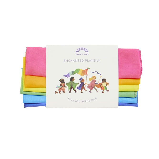 The Enchanted Playsilk by Sarahs Silks is a set of vibrant pink, green, yellow, and blue Rainbow Playsilks made from luxurious mulberry silk. The packaging features a label with an illustration of children engaged in imaginative play.