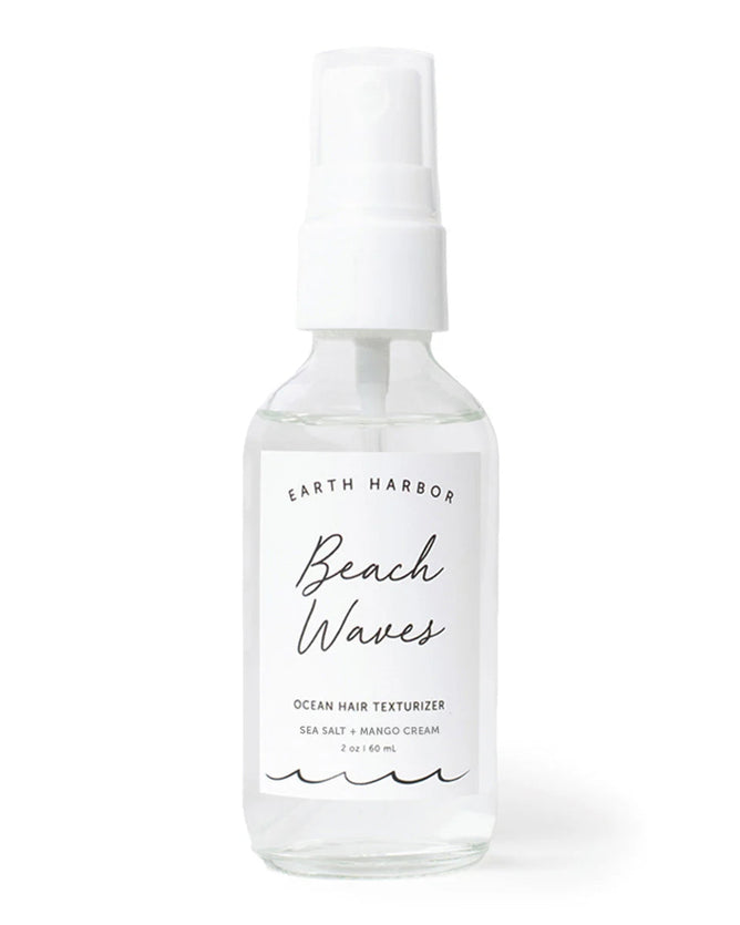 A clear spray bottle labeled BEACH WAVES Ocean Hair Texturizer by Earth Harbor rests against a plain background, containing vegan mango sea salt spray for the perfect beach style. It features a white nozzle and has a capacity of 2 oz / 60 mL.