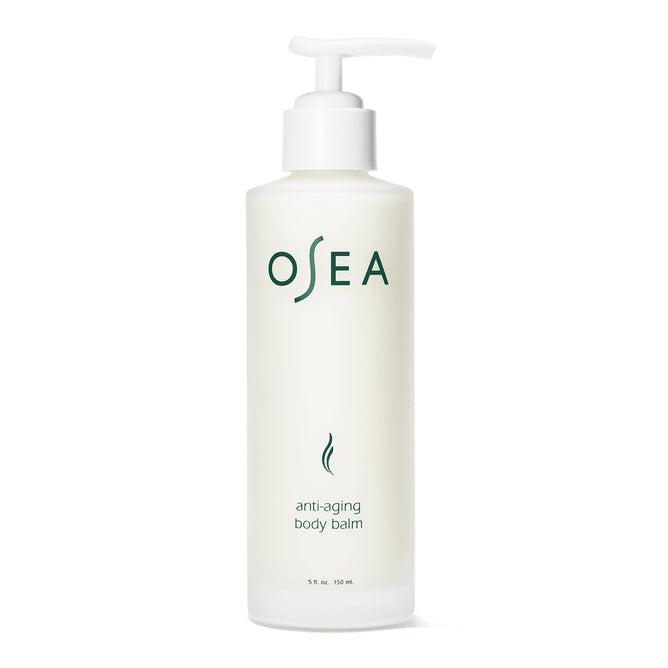 A white OSEA Anti-Aging Body Balm bottle with a pump dispenser boasts hydrating properties. Its label has green text and a minimalist wave design, exuding elegance and offering rejuvenating skincare.