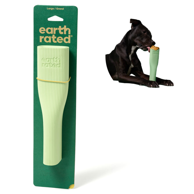The Earth Rated Natural Rubber Dog Enrichment Toy packaging highlights a large green toy, made from natural rubber and shaped like a ridged tube. To the right of the package, a black dog is shown enjoying the toy by gripping its ergonomic design with its mouth.