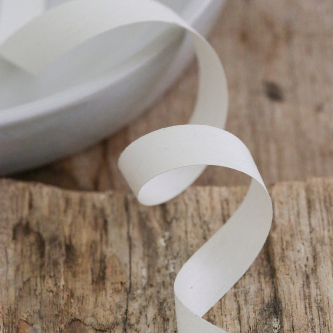 A sustainable ribbon from Waterleaf Paper Company elegantly drapes over a weathered wooden surface, partially resting on a white plate in the background.