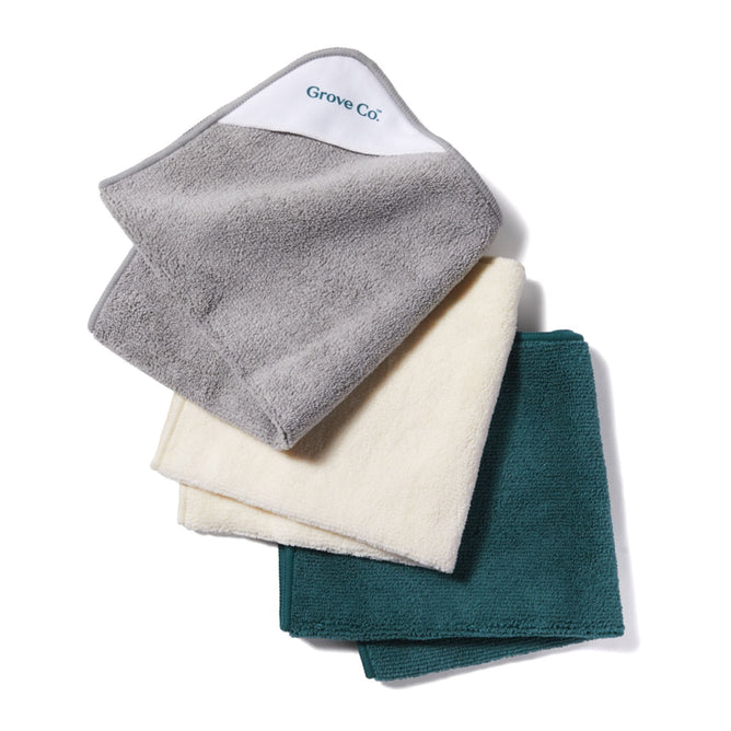A stack of three microfiber cleaning cloths, presented in gray, cream, and teal, showcases the Grove Co. brand on the top gray cloth. Made from eco-friendly and absorbent fibers.