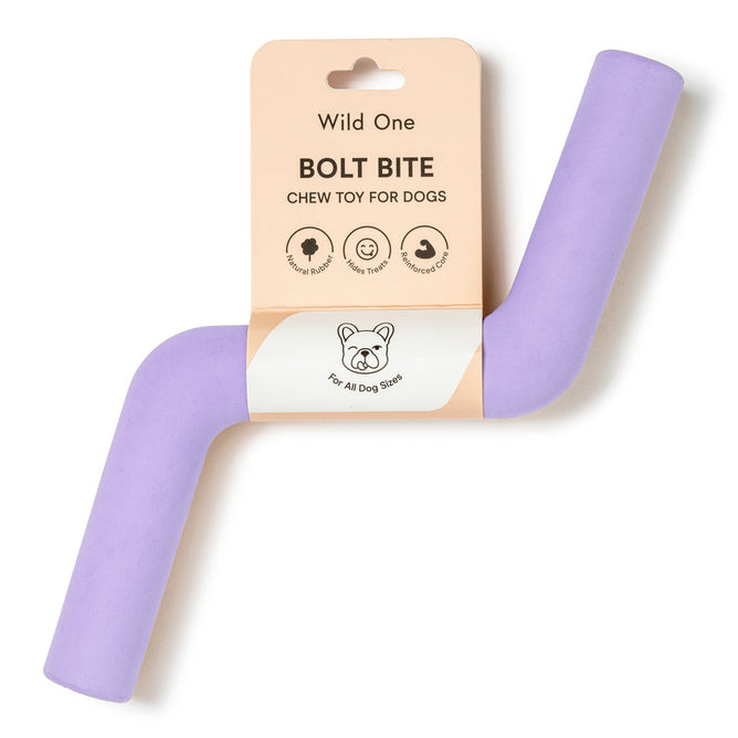 The Wild One Bolt Bite is a purple boomerang-shaped dog chew toy, crafted from natural rubber. Its dishwasher-safe, and the packaging features illustrations of a bottle, treat, and brush alongside For All Dog Sizes.