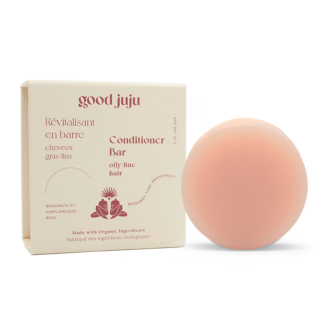 A round, peach-colored Volumizing Conditioner Bar by Good Juju Body & Home sits next to its beige box. Featuring red text in French and English, it highlights organic ingredients. Specially designed for oily, fine hair, it uses natural botanicals for a refreshing cleanse and lift.