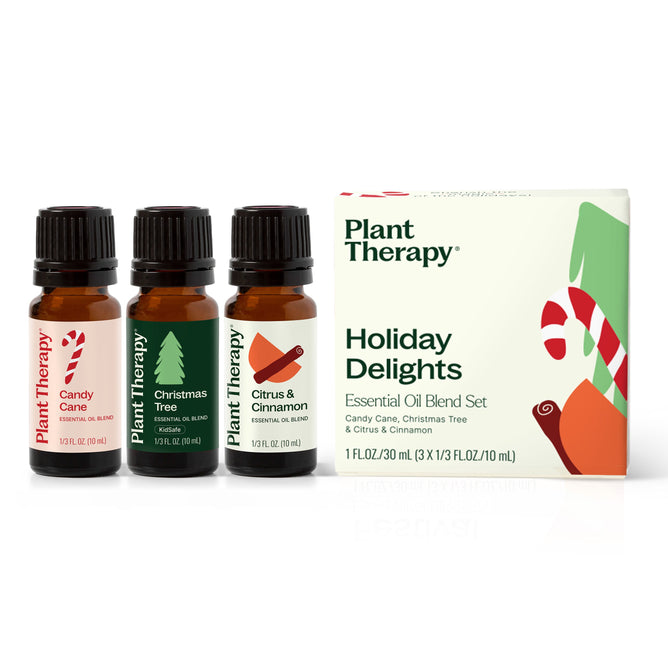 Three essential oils—Candy Cane blend, Christmas Tree blend, and Citrus & Cinnamon—are beautifully presented next to a festive white box labeled Plant Therapy Holiday Delights Essential Oil Blend Set, embodying holiday cheer.