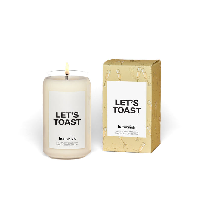 The Lets Toast candle by Homesick, made from natural soy wax, comes in a yellow box with champagne glass patterns. The box displays Lets Toast and Homesick. The glowing white wax evokes warmth like a distant handwritten note.