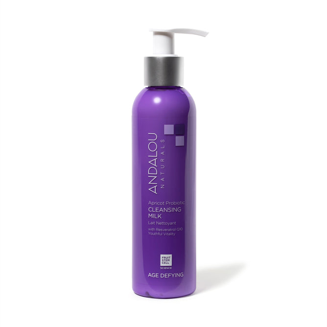 A purple bottle of Andalou Naturals Age Defying Apricot Probiotic Cleansing Milk features a white pump. The label highlights Age Defying with antioxidants for a healthy glow, making it ideal for dry skin. The bottle stands upright against a white background.