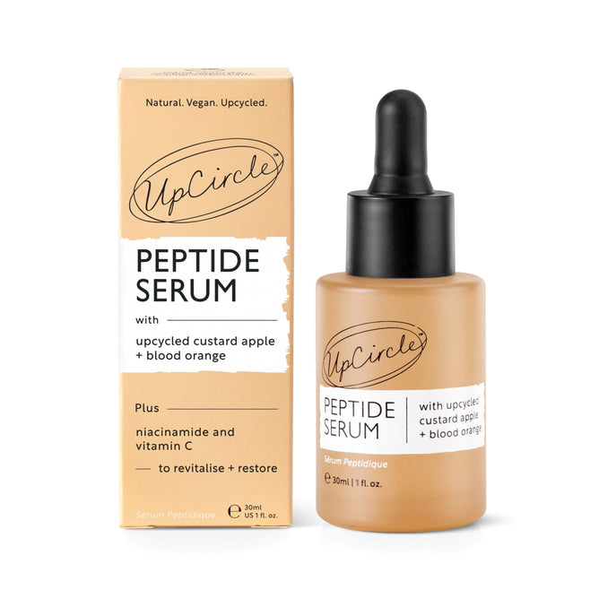 An UpCircle Peptide Serum with Custard Apple + Blood Orange bottle, complete with a dropper, stands next to its box. The label highlights upcycled custard apple, blood orange, niacinamide, and vitamin C. This natural and vegan serum is designed to enhance collagen production.