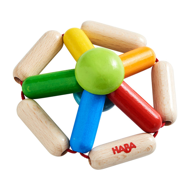 The Color Carousel Wooden Baby Rattle by HABA features green, yellow, red, and blue spokes radiating from a green center with beige cylinders. A red string weaves through the design, making it perfect for little ones. The HABA logo is printed on one piece.