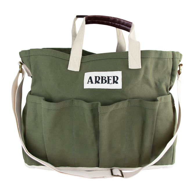 The Arber Garden Tote is a green canvas gardening bag featuring a spacious compartment, six exterior pockets, an adjustable shoulder strap, and short beige handles with a dark brown grip. It is adorned with a white ARBER label for style and comfort.