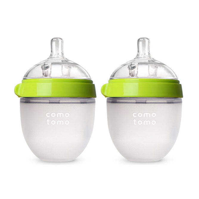 The Comotomo Baby Bottle 2-Pack, made from 100% food-grade silicone, includes two bottles with green lids and clear nipples. Featuring anti-colic vents, they are semi-transparent with measurement markings and designed with a wide mouth for easy cleaning and feeding.