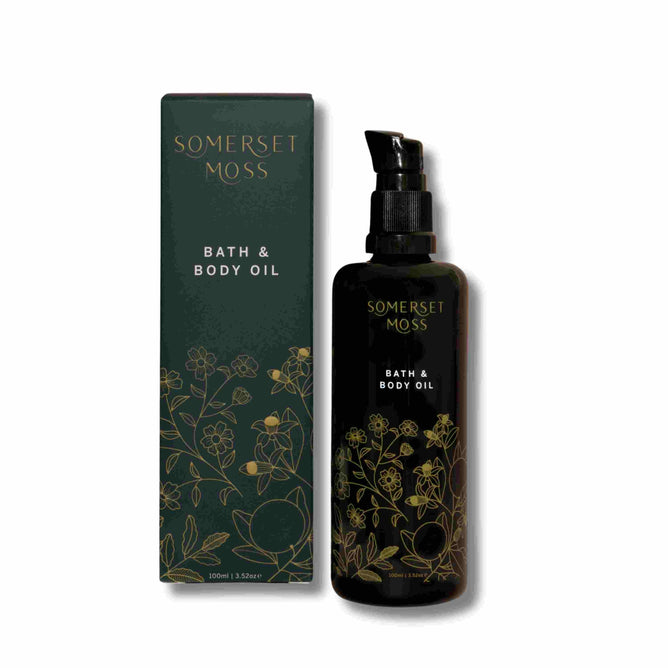 A dark green bottle of Somerset Moss Core Body Oil sits beside its matching box, both adorned with golden botanical illustrations, promising enhanced skin hydration. The product name is elegantly showcased on the box.