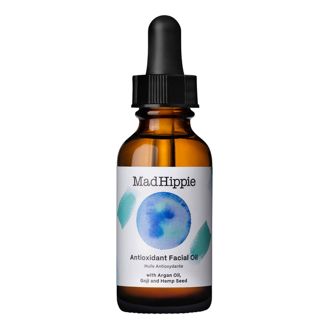 A brown glass dropper bottle labeled Mad Hippie Antioxidant Facial Oil features a blue circle with teal geometric shapes and contains natural ingredients such as argan oil, goji, and hemp seed, offering skin hydration with every drop.