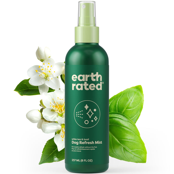 A 237 ml green bottle of Earth Rateds Deodorizing & Conditioning Refresh Mist for Dogs, scented with white tea and basil. It features a no-rinse solution and spray top, surrounded by white flowers and basil leaves.
