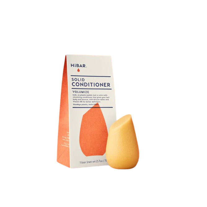 A yellow teardrop-shaped solid conditioner rests beside a white and orange box labeled HiBAR Volumize Conditioner. This eco-friendly product is specially designed to enhance body and volume in fine hair.