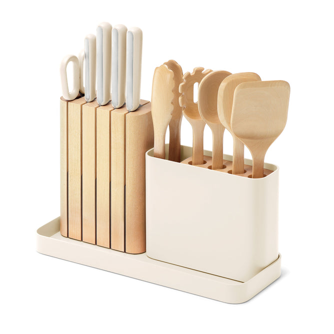 The Caraway 14-Piece Knife & Utensil Set features a cream-colored organizer made from FSC-certified birch wood, complete with a wooden knife block and various utensils such as spatulas and a pasta server. The design is compact and modern.