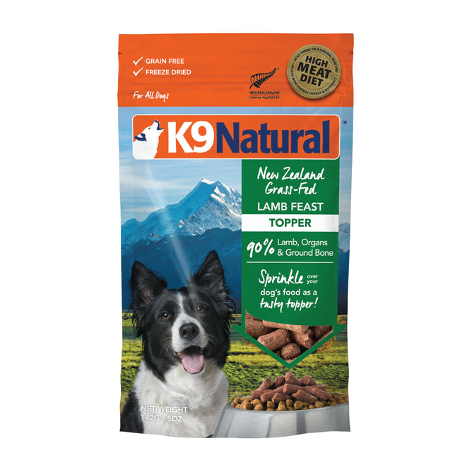 The K9 Natural Grain-Free Freeze-Dried Dog Food Topper packaging features a mountain scene with a black and white dog. It boasts premium New Zealand ingredients and is made from 90% lamb, organs, and ground bone—ideal as a nutritious meal booster for your dog.
