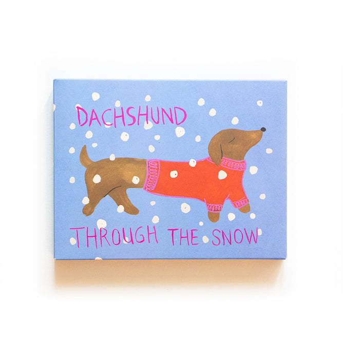 Illustrated dachshund in a red sweater on a blue snowflake background. Ideal for dog lovers, this Supra Endura Holiday Card reads Dachshund Through the Snow in pink and is printed on recycled paper.