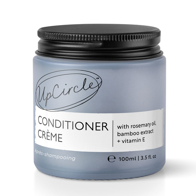 UpCircles Conditioner Crème, featuring rosemary oil, bamboo extract, and vitamin E, comes in a light blue 100 ml (3.5 fl oz) jar with a black lid.