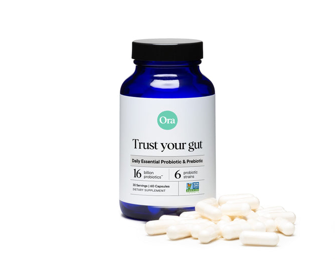 A blue bottle of Trust Your Gut Vegan Probiotics with Prebiotics by Ora Organic is set against a white background, highlighting its digestive health benefits. It contains 16 billion probiotics across 6 strains, with a few white capsules scattered in front.