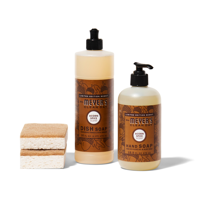 The Grove Collaborative crisp-clean-sinkside-set features two Acorn Spice Mrs. Meyers Clean Day bottles—one dish soap, one hand soap—beside stacked sponge scrubbers on a white background.